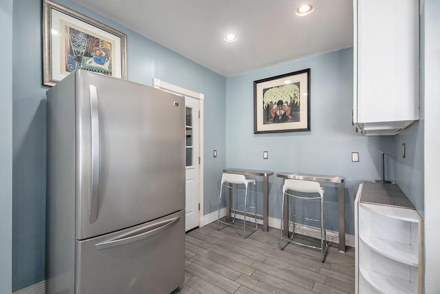 kitchen with freestanding refrigerator, white cabinetry, light wood-type flooring, baseboards, and recessed lighting