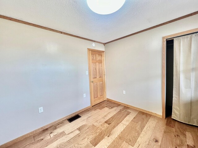 spare room with light wood finished floors, crown molding, visible vents, baseboards, and a textured ceiling