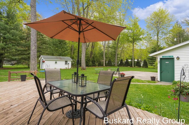 1127 Wolf Lake Dr, Baldwin, MI 49304 - wooden terrace featuring an outbuilding, outdoor dining area, a lawn, and view of wooded area