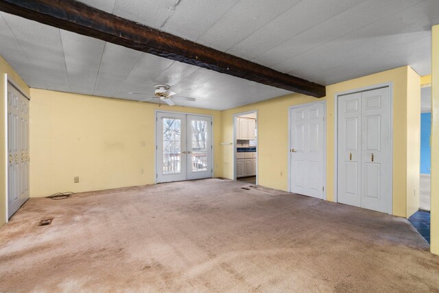 unfurnished living room featuring a ceiling fan, visible vents, carpet floors, french doors, and beamed ceiling