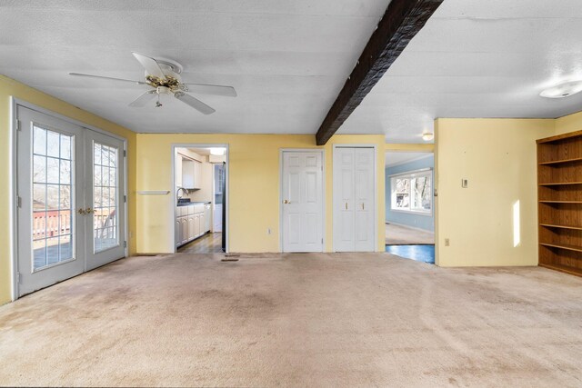 unfurnished living room featuring french doors, carpet floors, beam ceiling, and ceiling fan
