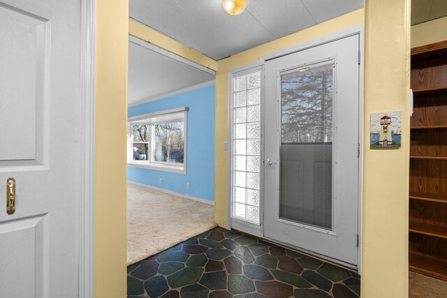entryway featuring crown molding, baseboards, and dark colored carpet
