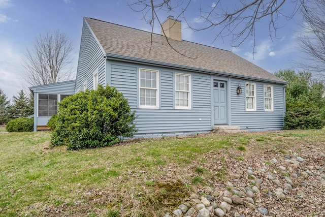 view of front of house with a front yard, a sunroom, roof with shingles, and a chimney