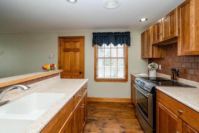 kitchen featuring stainless steel electric range oven, a sink, decorative backsplash, light countertops, and brown cabinets