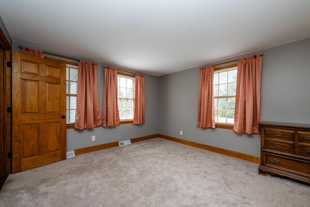 unfurnished bedroom with visible vents, multiple windows, baseboards, and carpet floors