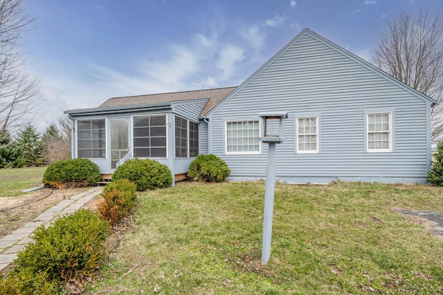 rear view of house featuring a lawn, a shingled roof, and a sunroom