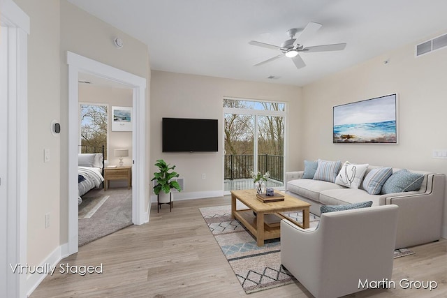living room featuring a ceiling fan, visible vents, light wood finished floors, and baseboards