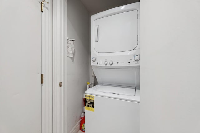 laundry area with baseboards, stacked washer / dryer, and laundry area