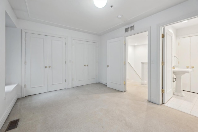 unfurnished bedroom with two closets, visible vents, connected bathroom, and carpet