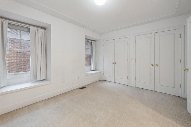unfurnished bedroom featuring carpet flooring, multiple windows, two closets, and visible vents