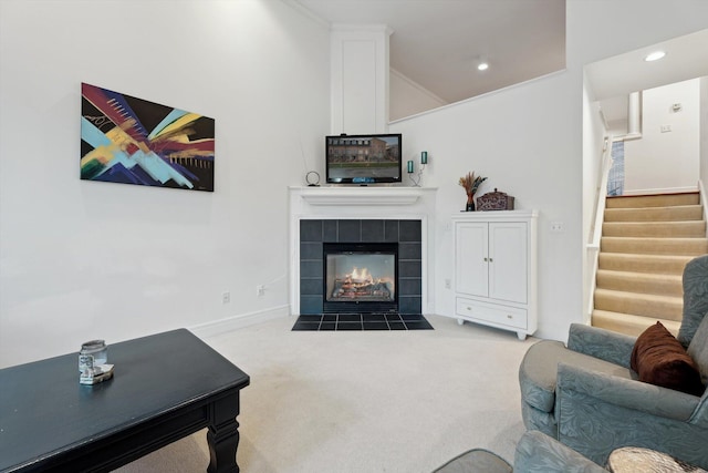 living area with stairs, vaulted ceiling, a tile fireplace, carpet flooring, and baseboards