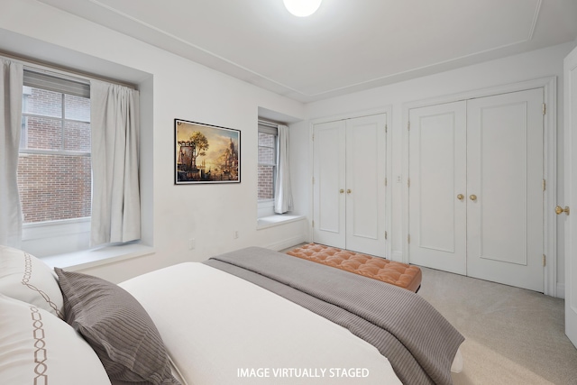 bedroom featuring light colored carpet and multiple closets