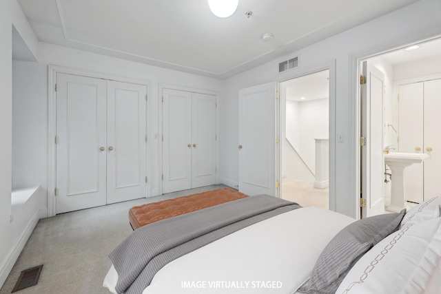 bedroom with light colored carpet, visible vents, multiple closets, and a sink