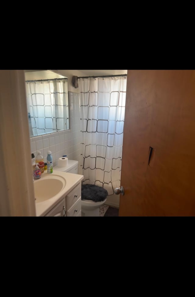 bathroom with tasteful backsplash, toilet, vanity, a shower with shower curtain, and tile walls