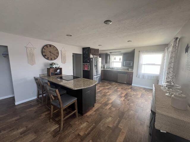 2772 S Wisner Ave, Fremont, MI 49412 - kitchen featuring baseboards, a peninsula, black appliances, dark wood-type flooring, and a kitchen breakfast bar
