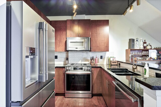 kitchen featuring tasteful backsplash, a sink, light wood finished floors, a peninsula, and appliances with stainless steel finishes