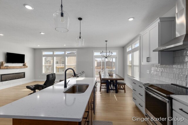 5560 Albright Ave SW Unit 67, Wyoming, MI 49418 - kitchen featuring tasteful backsplash, electric stove, a sink, a glass covered fireplace, and wall chimney exhaust hood