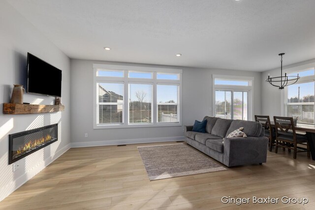 5560 Albright Ave SW Unit 67, Wyoming, MI 49418 - living area featuring light wood-style flooring, baseboards, recessed lighting, a glass covered fireplace, and an inviting chandelier