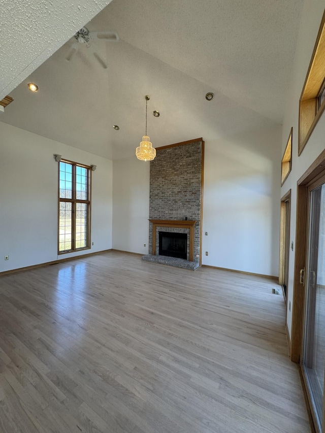 unfurnished living room featuring a fireplace, baseboards, high vaulted ceiling, a textured ceiling, and light wood finished floors