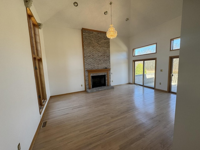 unfurnished living room with visible vents, a towering ceiling, wood finished floors, a fireplace, and baseboards