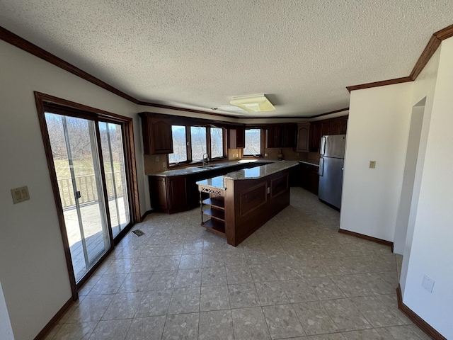 kitchen featuring freestanding refrigerator, ornamental molding, a kitchen island, dark brown cabinets, and a textured ceiling