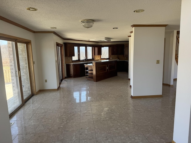 kitchen featuring dark brown cabinets, a textured ceiling, a center island, baseboards, and ornamental molding