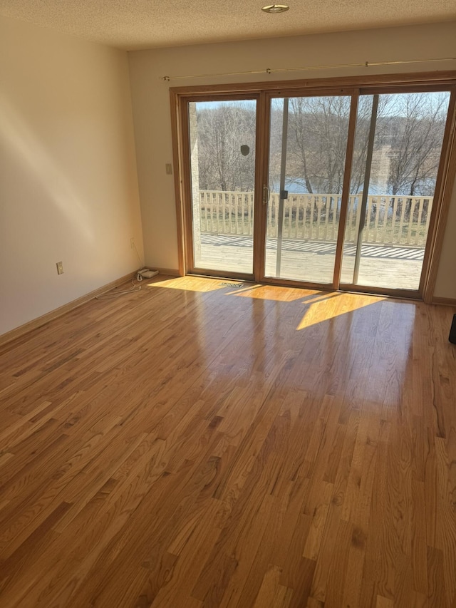 unfurnished room featuring a textured ceiling, baseboards, and wood finished floors