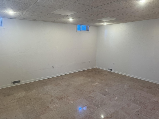 finished below grade area featuring tile patterned floors, baseboards, a drop ceiling, and visible vents