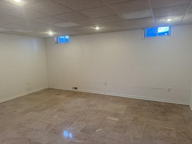 below grade area with tile patterned floors, visible vents, baseboards, and a paneled ceiling