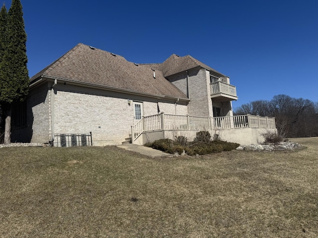 view of side of property with brick siding, a lawn, roof with shingles, and a balcony
