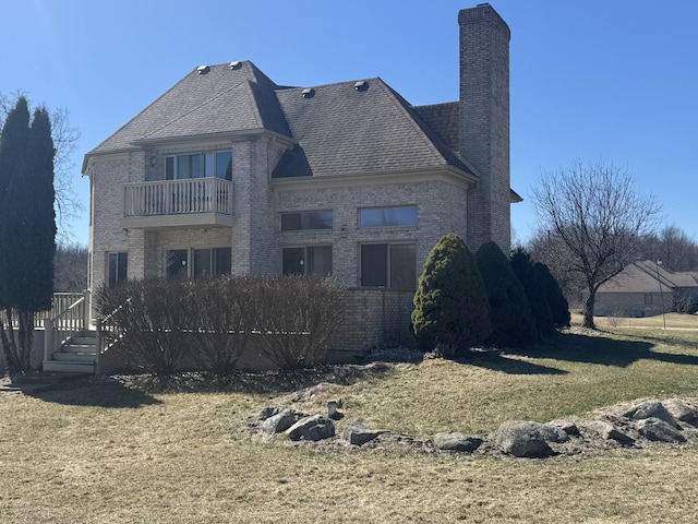 back of house with a lawn, brick siding, a chimney, and a balcony