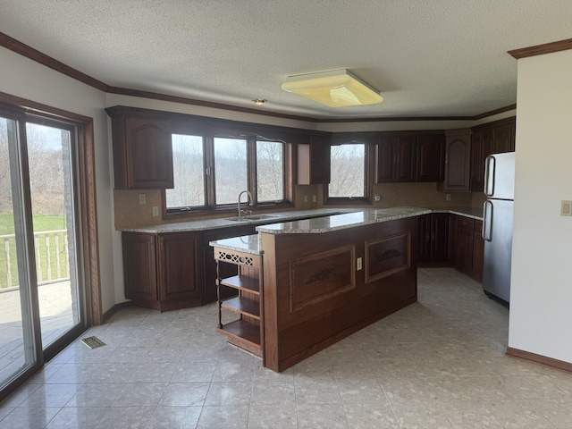kitchen with a sink, a center island, freestanding refrigerator, and a healthy amount of sunlight