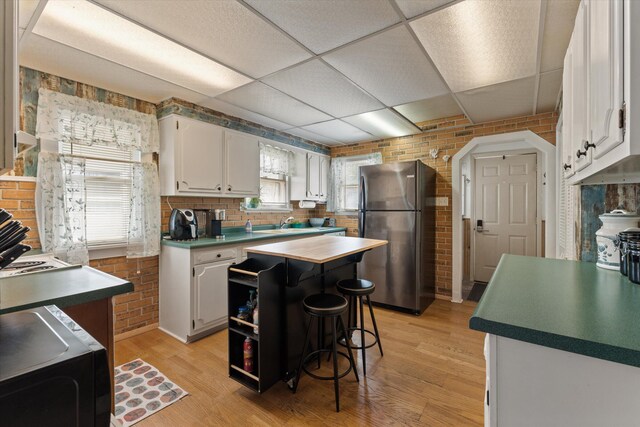 1169 Shady Shores Dr, Niles, MI 49120 - kitchen with white cabinetry, brick wall, a drop ceiling, and freestanding refrigerator