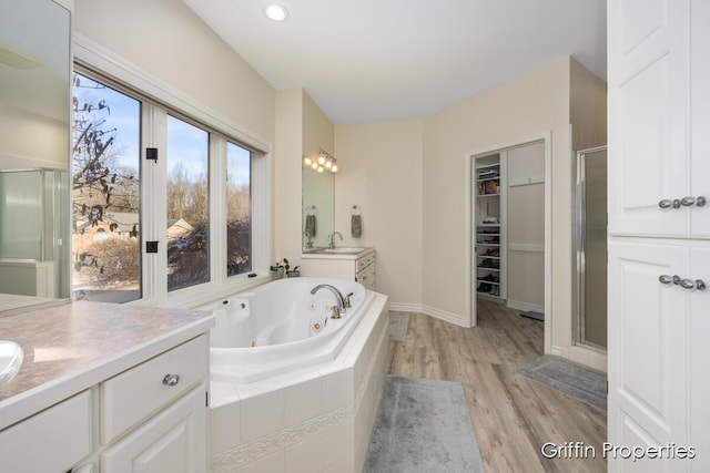 7834 Strawberry Ln NE, Belmont, MI 49306 - bathroom featuring two vanities, a stall shower, a sink, wood finished floors, and a tub with jets