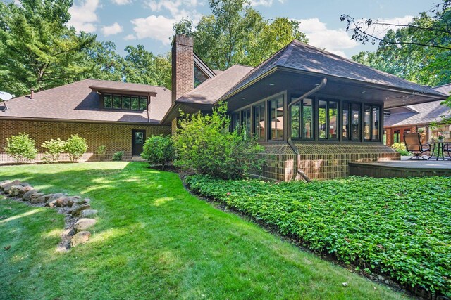 4923 Hickory Hill Rd, Ann Arbor, MI 48105 - rear view of house with a sunroom, roof with shingles, brick siding, a yard, and a chimney