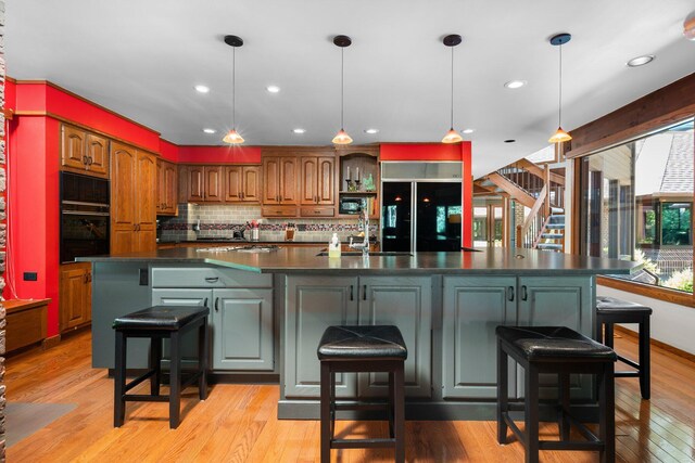 4923 Hickory Hill Rd, Ann Arbor, MI 48105 - kitchen with a large island with sink, light wood-type flooring, backsplash, dark countertops, and black appliances