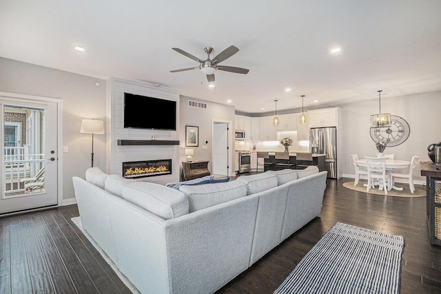 living room with dark wood-style flooring, a large fireplace, visible vents, and a ceiling fan
