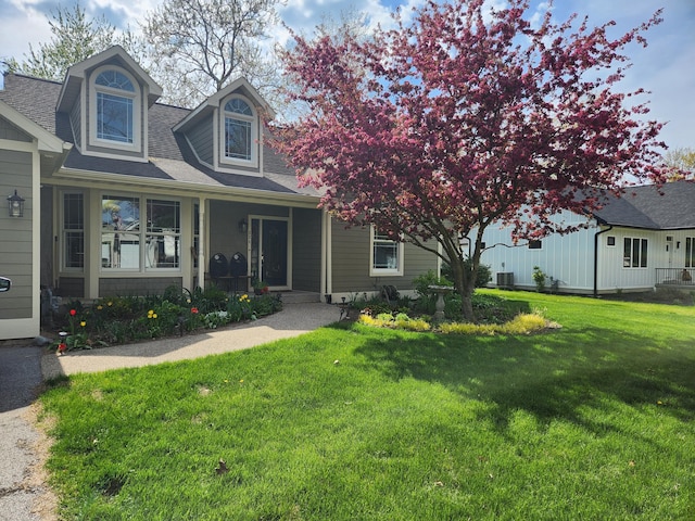view of front of home with a front yard, a porch, cooling unit, and roof with shingles