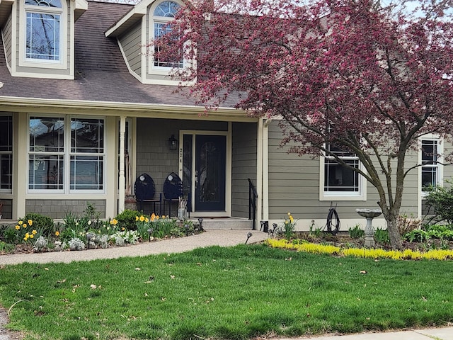 view of exterior entry with a porch, a lawn, and roof with shingles