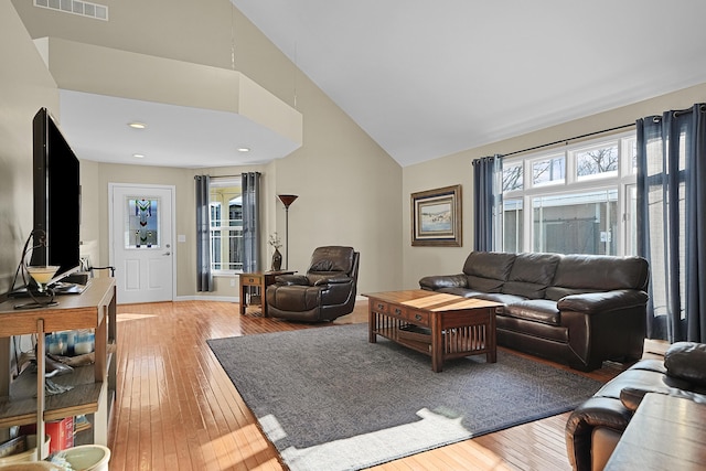 living area featuring visible vents, plenty of natural light, high vaulted ceiling, and light wood-style flooring