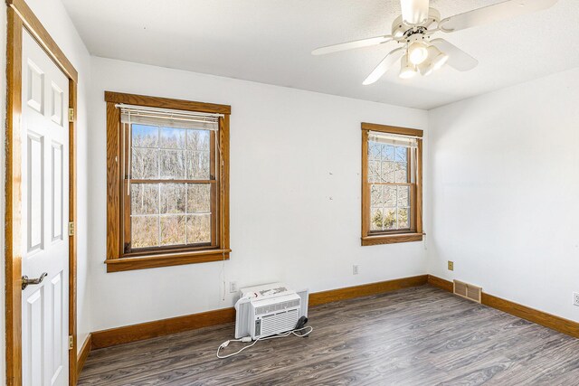 unfurnished room with baseboards, visible vents, a wall mounted air conditioner, and dark wood-style flooring