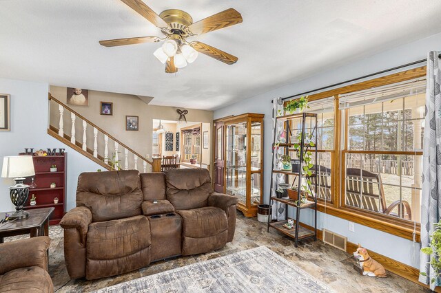 living area featuring stairs, baseboards, visible vents, a ceiling fan, and stone finish flooring