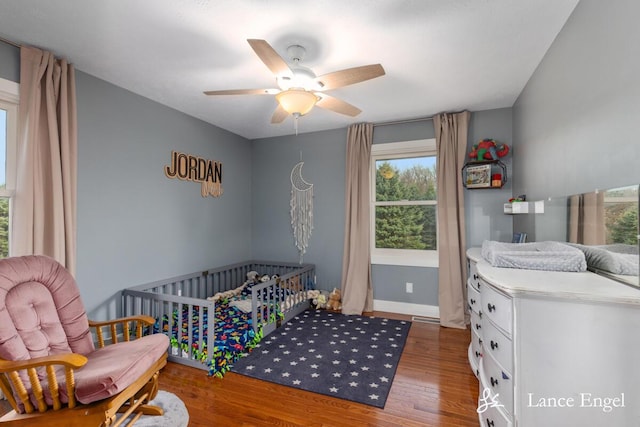 bedroom featuring baseboards, ceiling fan, wood finished floors, and multiple windows