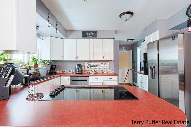 kitchen with a peninsula, white cabinetry, stainless steel appliances, and a sink