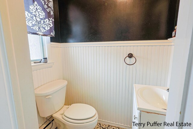 half bathroom with vanity, toilet, and a wainscoted wall