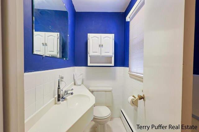 bathroom with a sink, toilet, tile walls, wainscoting, and baseboard heating
