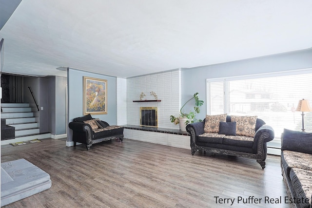 living area featuring wood finished floors, stairs, a baseboard heating unit, a fireplace, and baseboards