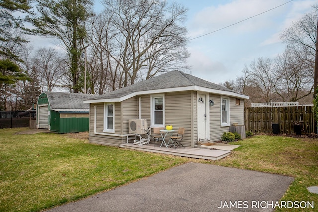 exterior space with fence, a shingled roof, an outdoor structure, ac unit, and a front yard