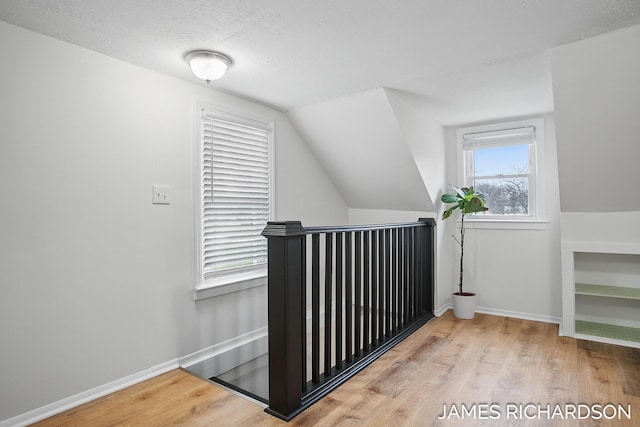 additional living space featuring baseboards, vaulted ceiling, wood finished floors, and a textured ceiling