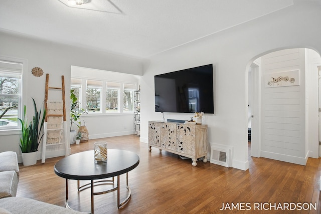 living area with plenty of natural light, wood finished floors, visible vents, and arched walkways
